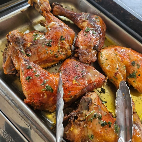 Close-up of golden-brown roasted chicken pieces with herbs and sauce in a metal tray.