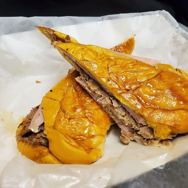 A Cuban sandwich from Tom's Cuban on the Go, cut in half, revealing layers of meat.