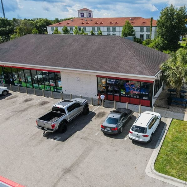 Aerial view of Tom's Cuban on the Go restaurant with parked cars and a distant building.