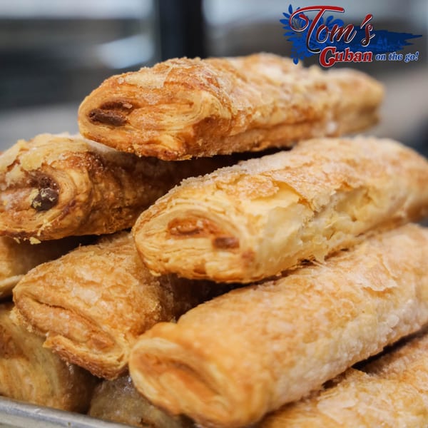 A close-up of golden-brown, sugar-dusted Cuban pastries, stacked on a tray.