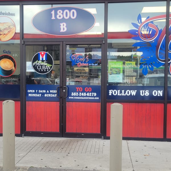 The red and blue storefront of Tom's Cuban on the Go, with signs for authentic Cuban food.