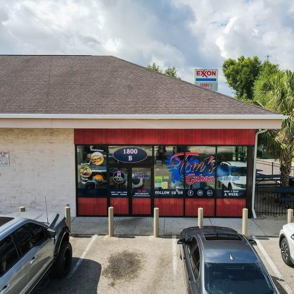 Exterior of Tom's Cuban on the Go, a red and white building with a parking lot and cars.