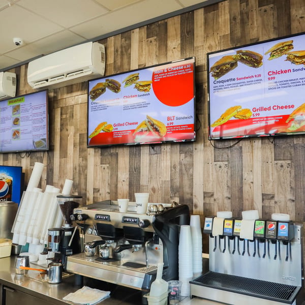 A Cuban restaurant counter with menu screens displaying sandwiches, a coffee machine, and a soda fountain.