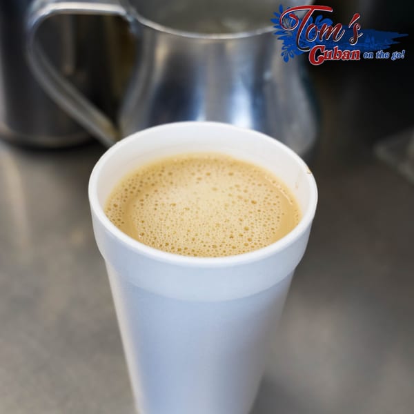 A white styrofoam cup of frothy Cuban coffee sits on a metal counter at Tom's Cuban on the Go.