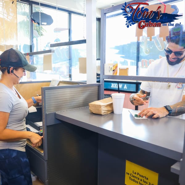 Two Tom's Cuban on the Go employees, one serving a customer, the other at a register.