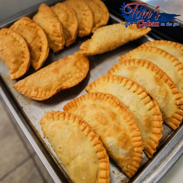 Golden-brown Cuban empanadas, arranged in rows on a metal baking sheet, ready to be served.